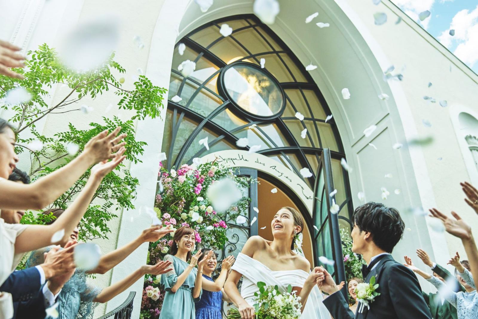 笑顔溢れる、祝福のフラワーシャワー。緑豊かなガーデンでは写真タイムやバルーンリリースなども叶う。「天使が見守る教会」ガラス張りの扉の上には、コンセプトの天使が描かれている