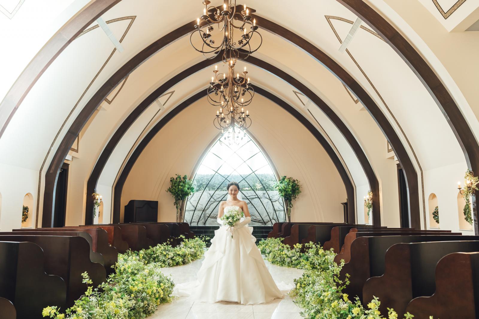 天然木の温もりと正面の大きな窓から自然光が降り注ぐ落ち着いた空間。20mものバージンロードと黒い大理石の祭壇でウェディングドレス姿をより一層美しく魅せる。